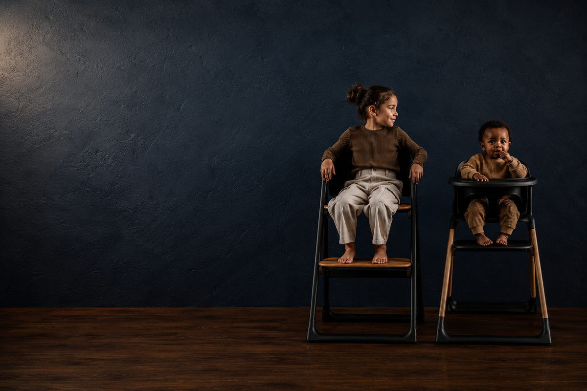 Child seated in the black Alto highchair beside a baby in the black Luna highchair with tray, both with feet resting on their footrests.