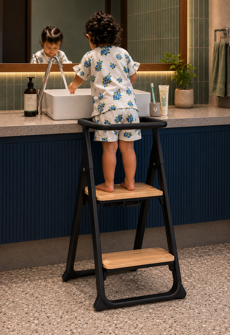 Black Alto Learning Tower with wooden steps and safety rail, supporting a child washing their hands at a bathroom sink.