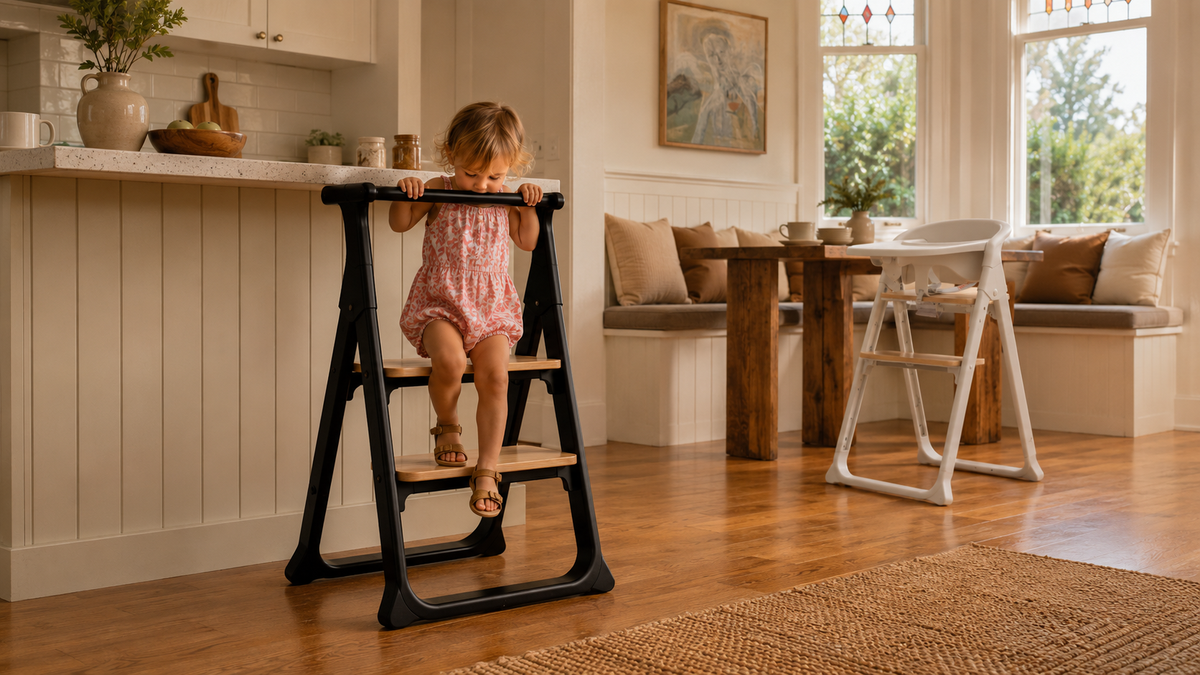 Child climbing down a black Alto learning tower with natural wood platforms, with a white Alto highchair beside the dining table in the background.