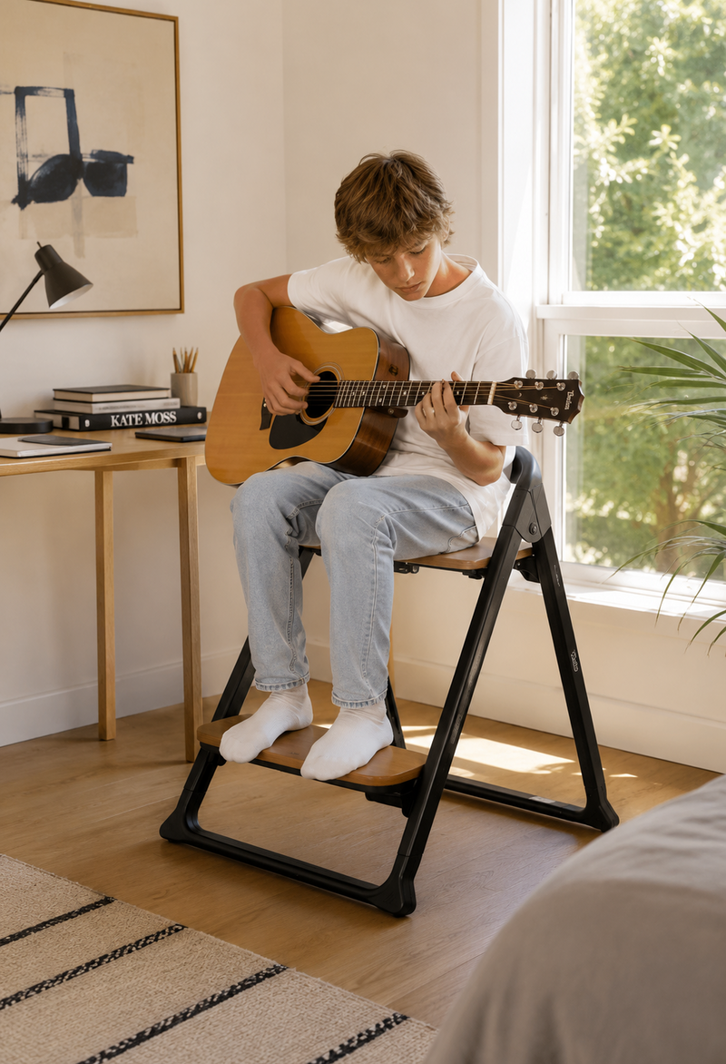Alto Complete Highchair System in black, configured as a chair with a teenager seated playing guitar.