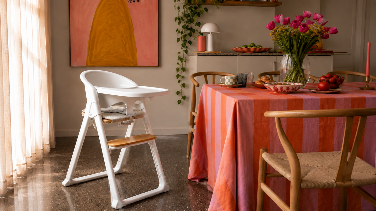 White Alto highchair with tray, toddler safety rail and cushion, showing the wooden seat and adjustable footplate beside a dining table.