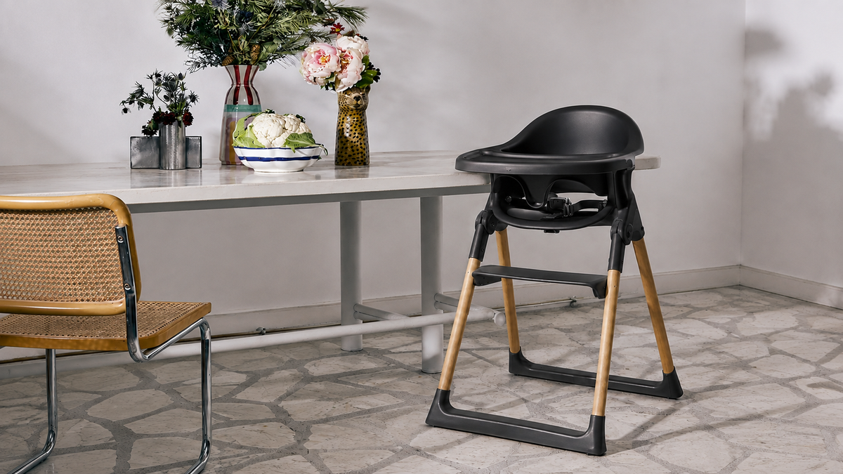 Black Luna highchair with tray, toddler safety rail and harness, showing natural wooden legs and adjustable footrest beside a dining table.